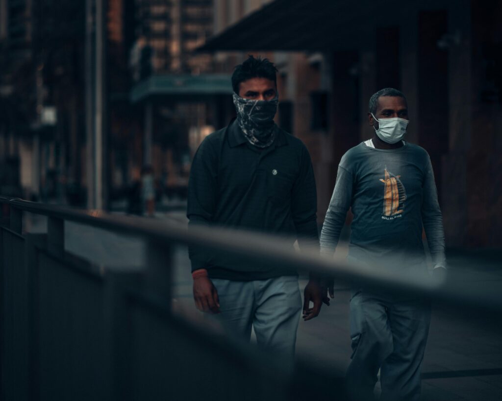 Two men wearing masks walk through a dimly lit street in Dubai, creating a somber urban scene.